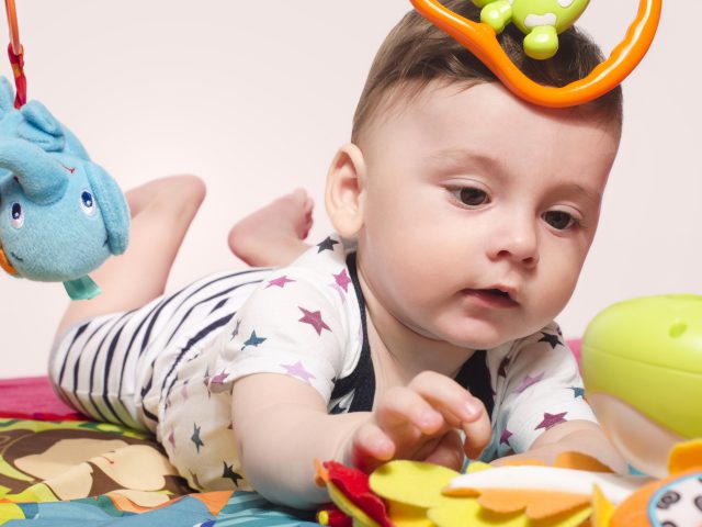 Cute baby boy sitting on a playmat and playing with toys. Adorable six month old child happy crawling to reach the toys.